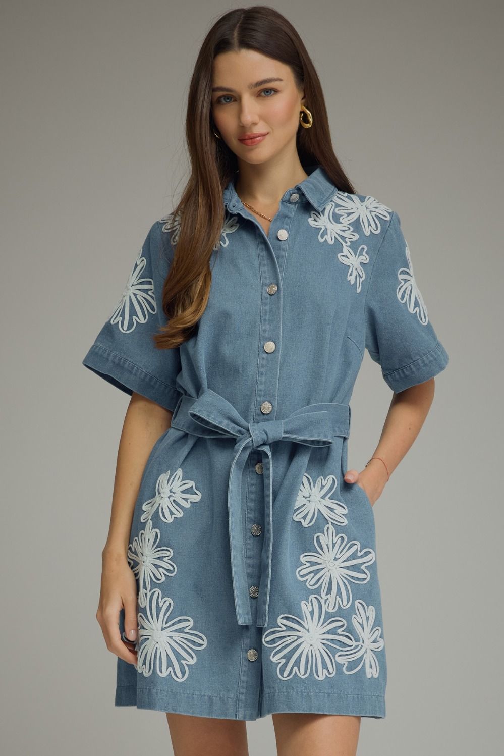 Light blue denim shirt dress with white embroidered daisy detail, denim tie belt, button-front closure, and A-line silhouette hitting at knee length.