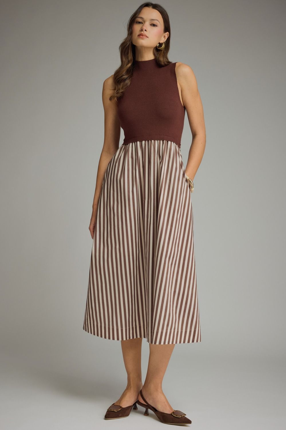 Brown sweater knit and striped midi dress with mock-neck neckline, sleeveless construction, brown and ecru vertical stripes on woven skirt, A-line silhouette, hits mid-calf.