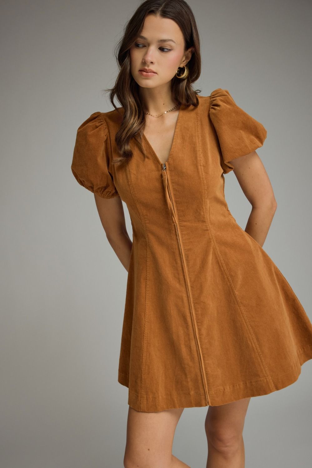 Camel-colored mini dress with V-neckline, short puffed sleeves with elasticated cuffs, fitted bodice, A-line skirt, front zipper closure, and side pockets.