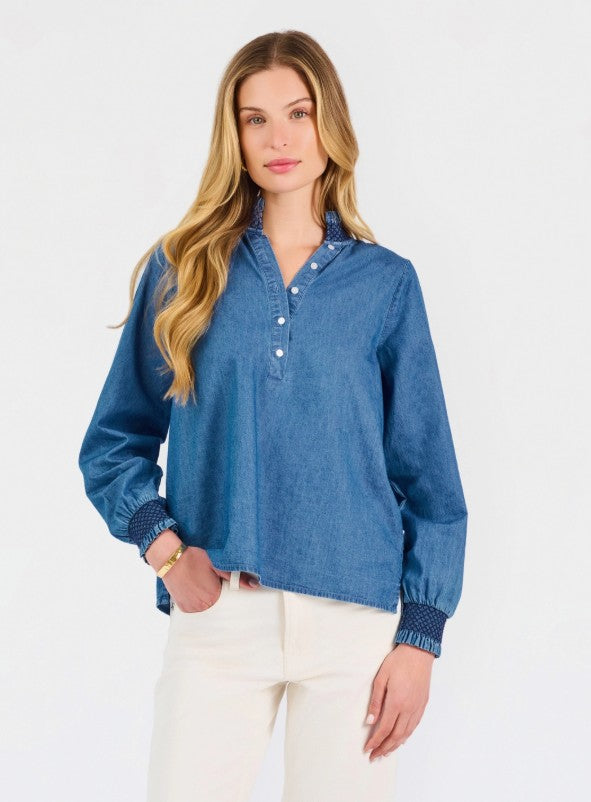 Medium blue chambray pullover top with collared neckline, half-button placket front, long sleeves with textured ribbed cuffs, and curved hemline hitting at hip.
