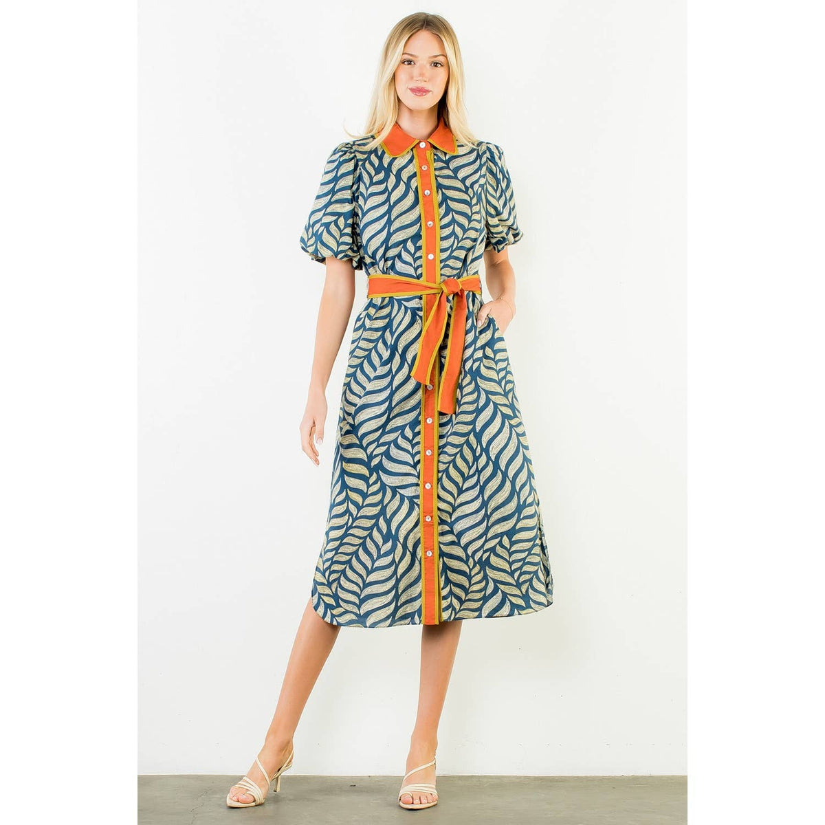 Model wearing a navy and pale green leaf-print midi dress with short puff sleeves, an orange collar, button front, and matching tie belt.