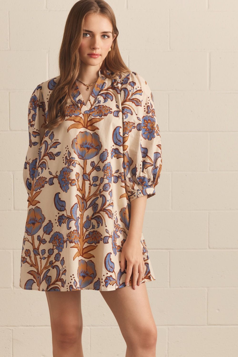 Model wearing an ecru floral mini shift dress with blue and brown botanical motifs, a split neckline, and three-quarter puff sleeves.