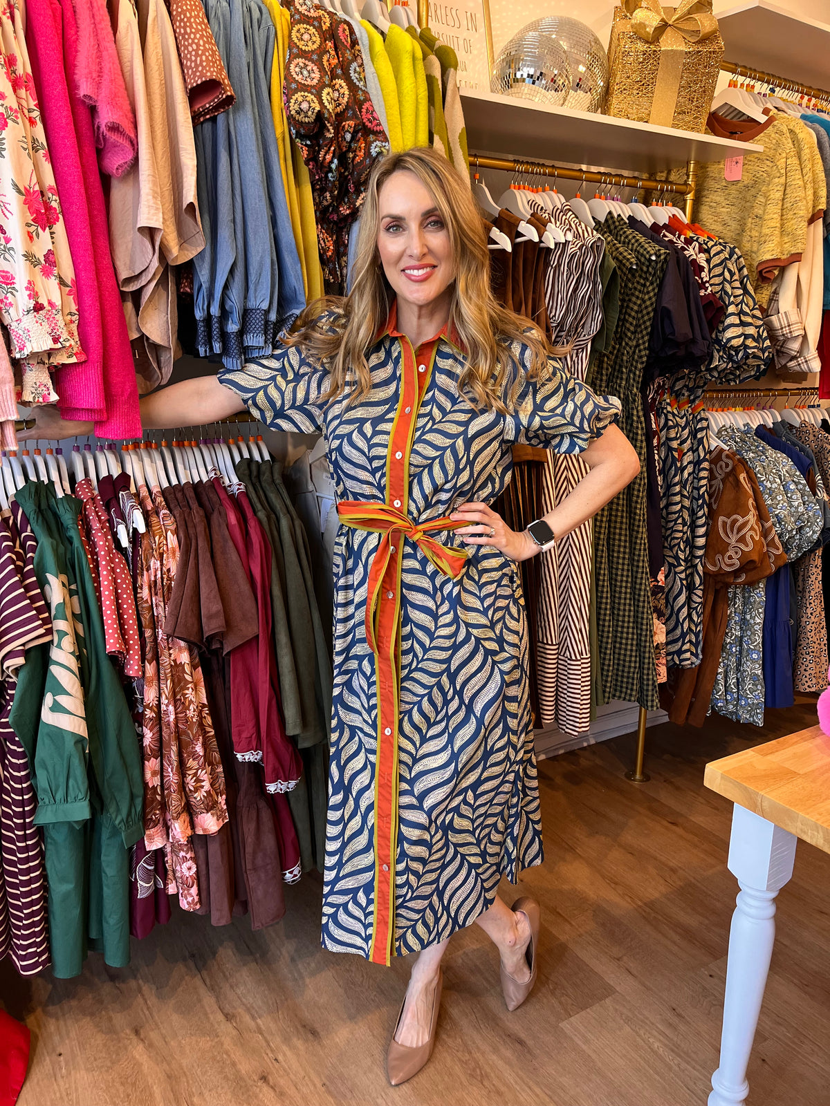 Model wearing a navy and pale green leaf-print midi dress with short puff sleeves, an orange collar, button front, and matching tie belt.