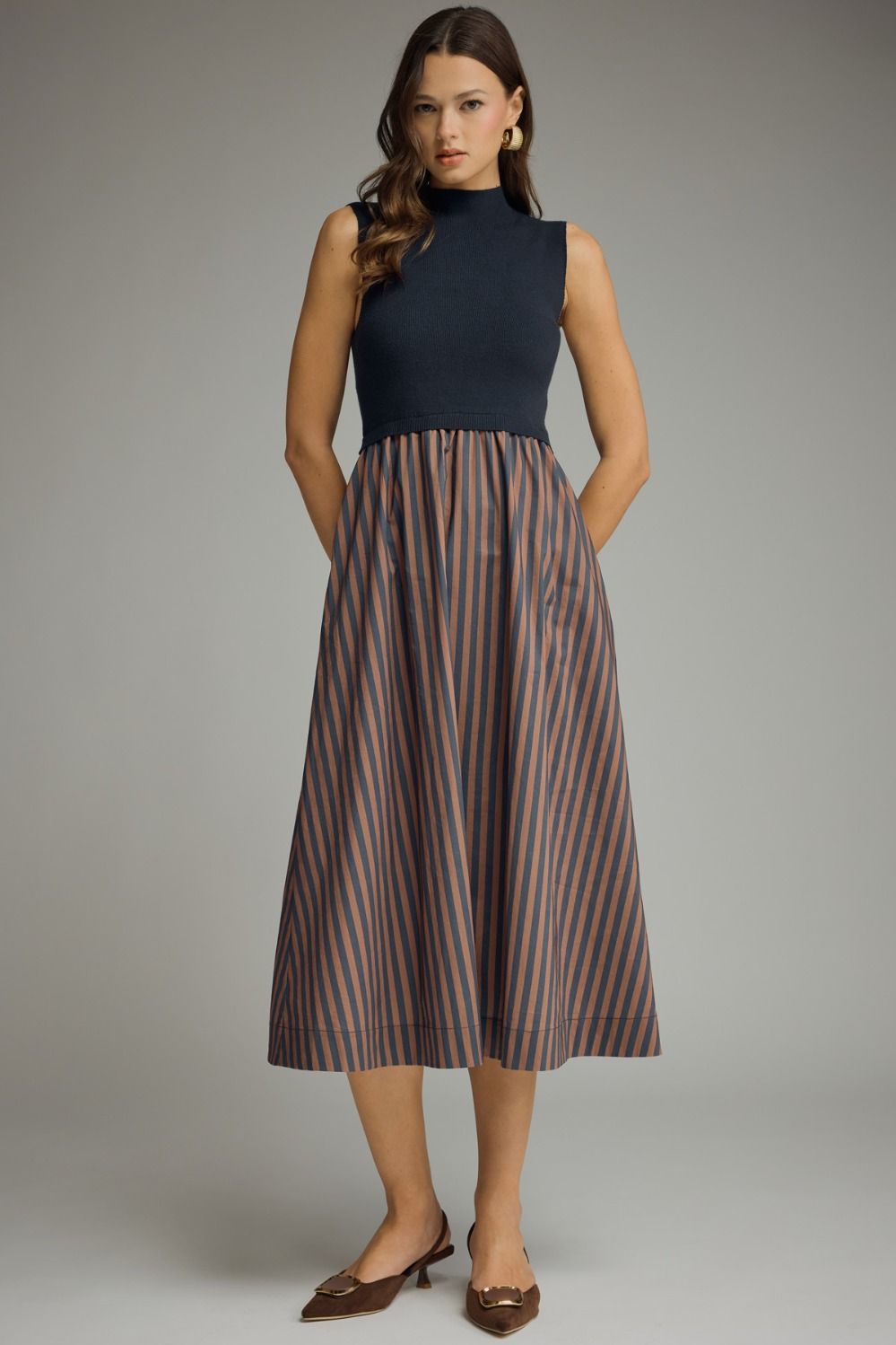 Navy sweater knit and striped midi dress with mock-neck neckline, sleeveless construction, brown and navy vertical stripes on woven skirt, A-line silhouette, hits mid-calf.