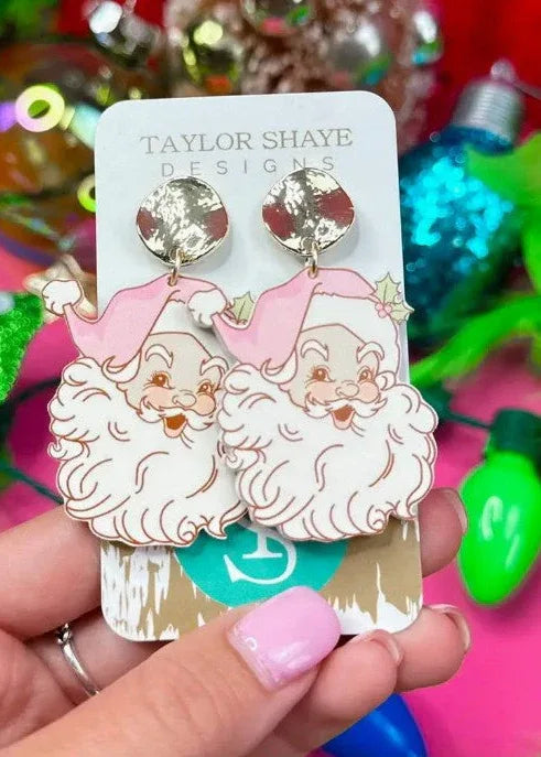 Acrylic Santa face drop earrings with pink hats, white beards, and textured round gold-tone tops, displayed on a jewelry card.⠋