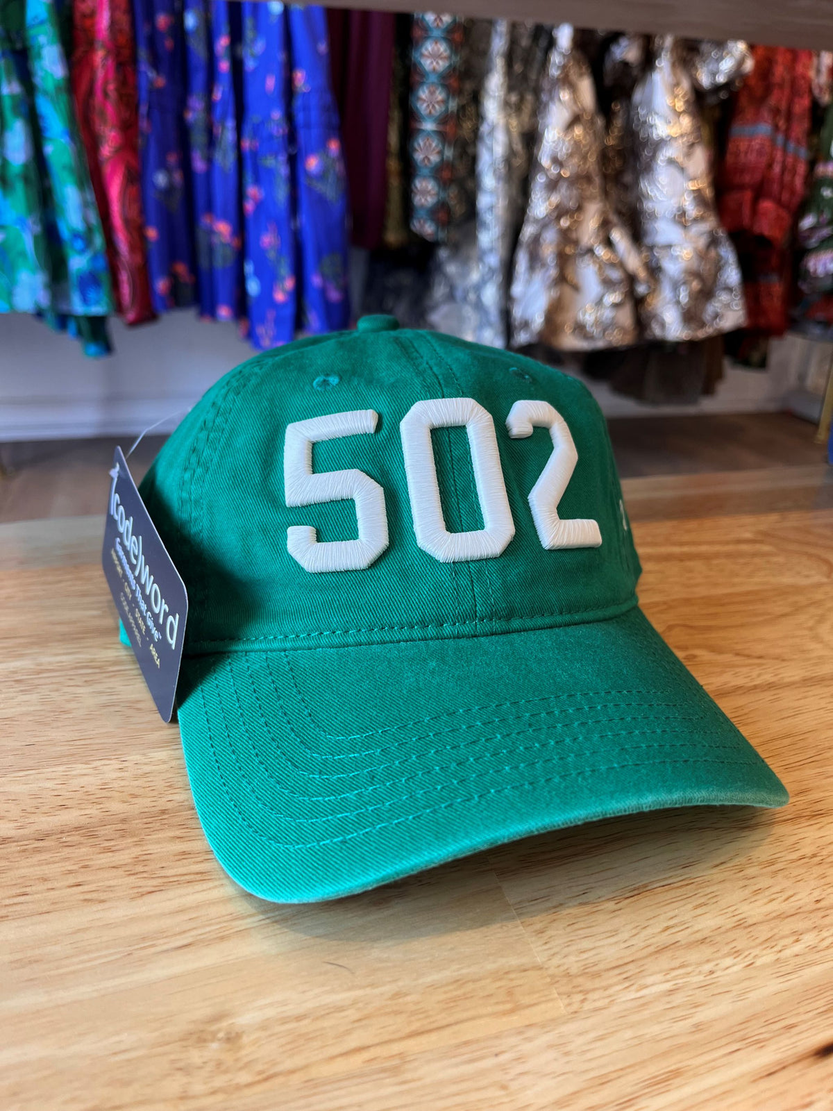 Green baseball cap with raised white 502 area code embroidery and a curved brim, displayed on a wooden surface.”
