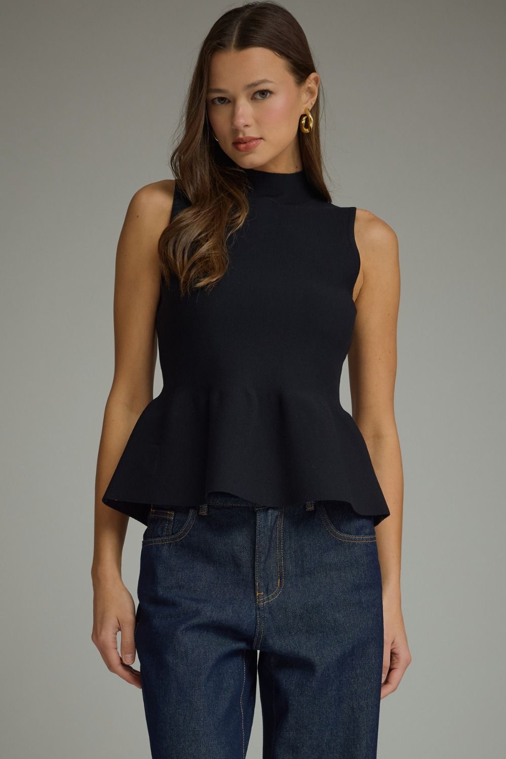 Black mock neck sleeveless sweater knit top with fitted bodice and structured peplum ruffle at waist.