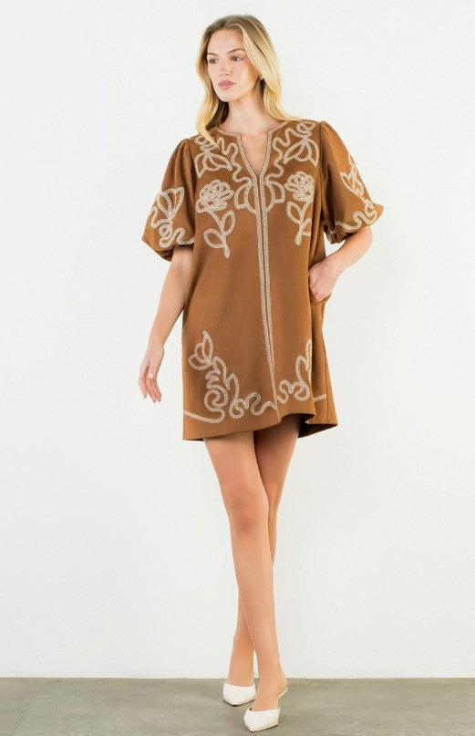 Brown tunic dress with cream embroidered botanical motifs on front, back, and sleeves, V-neckline, center front zip closure, short flutter sleeves, relaxed A-line silhouette, slightly curved asymmetric hem, knee length.