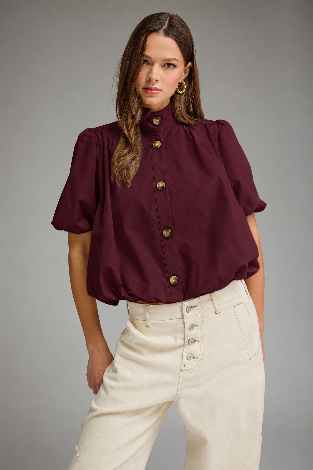 Model wearing a wine puff sleeve top with a band collar, button front, and bubble hem, paired with cream jeans.