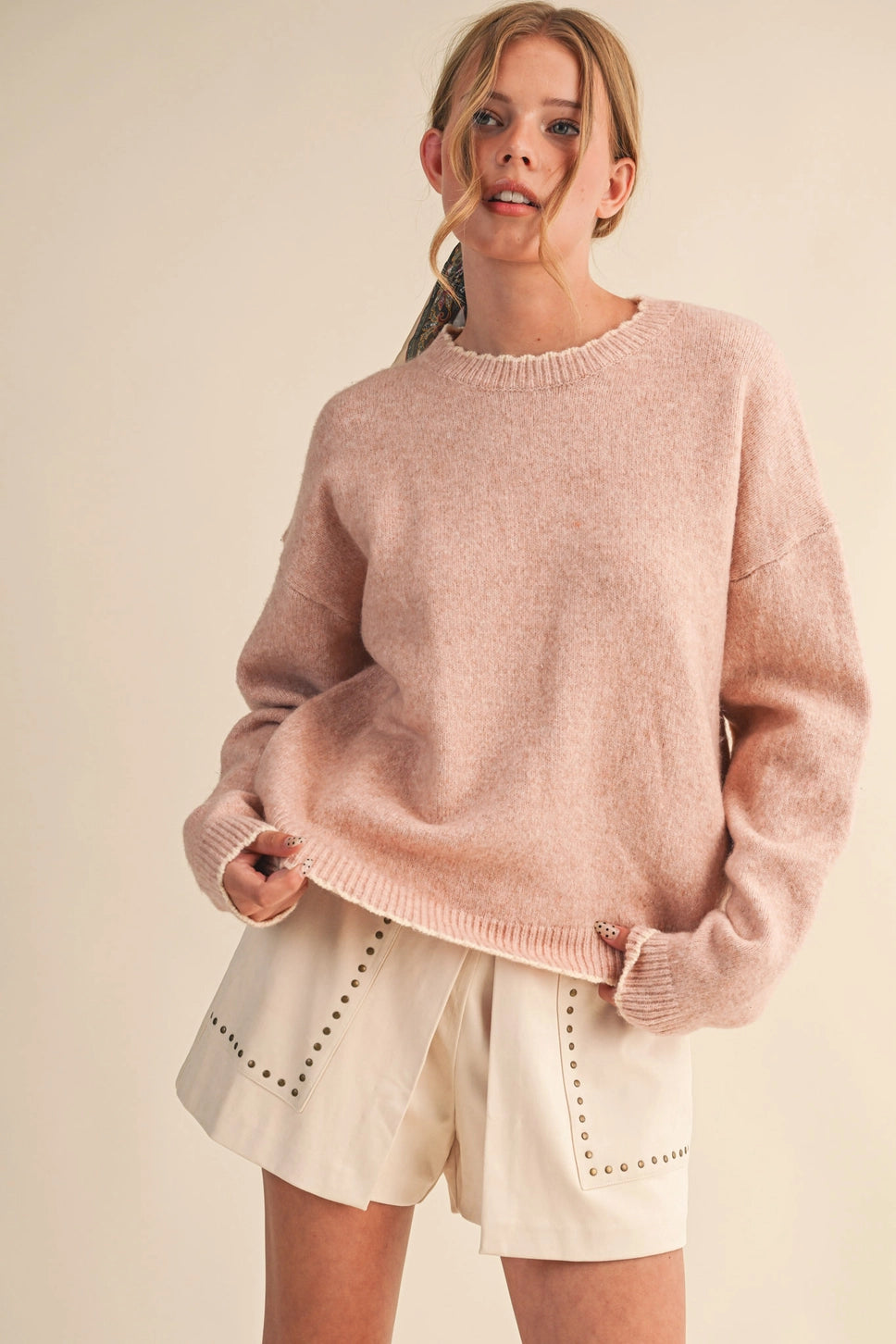 Model wearing a dusty pink crewneck sweater with a relaxed fit, long sleeves, and ribbed neckline, cuffs, and hem