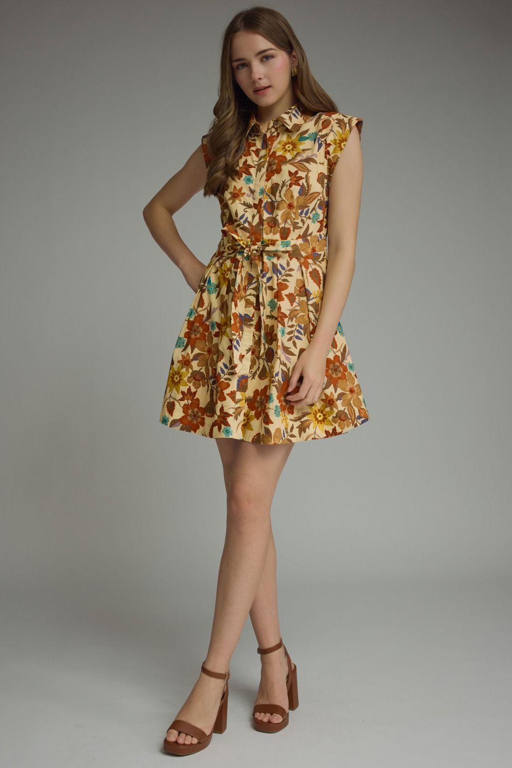 Cream retro floral cotton belted mini shirtdress with point collar, sleeveless silhouette, button-down front, and self-tie waist on model with block heel sandals