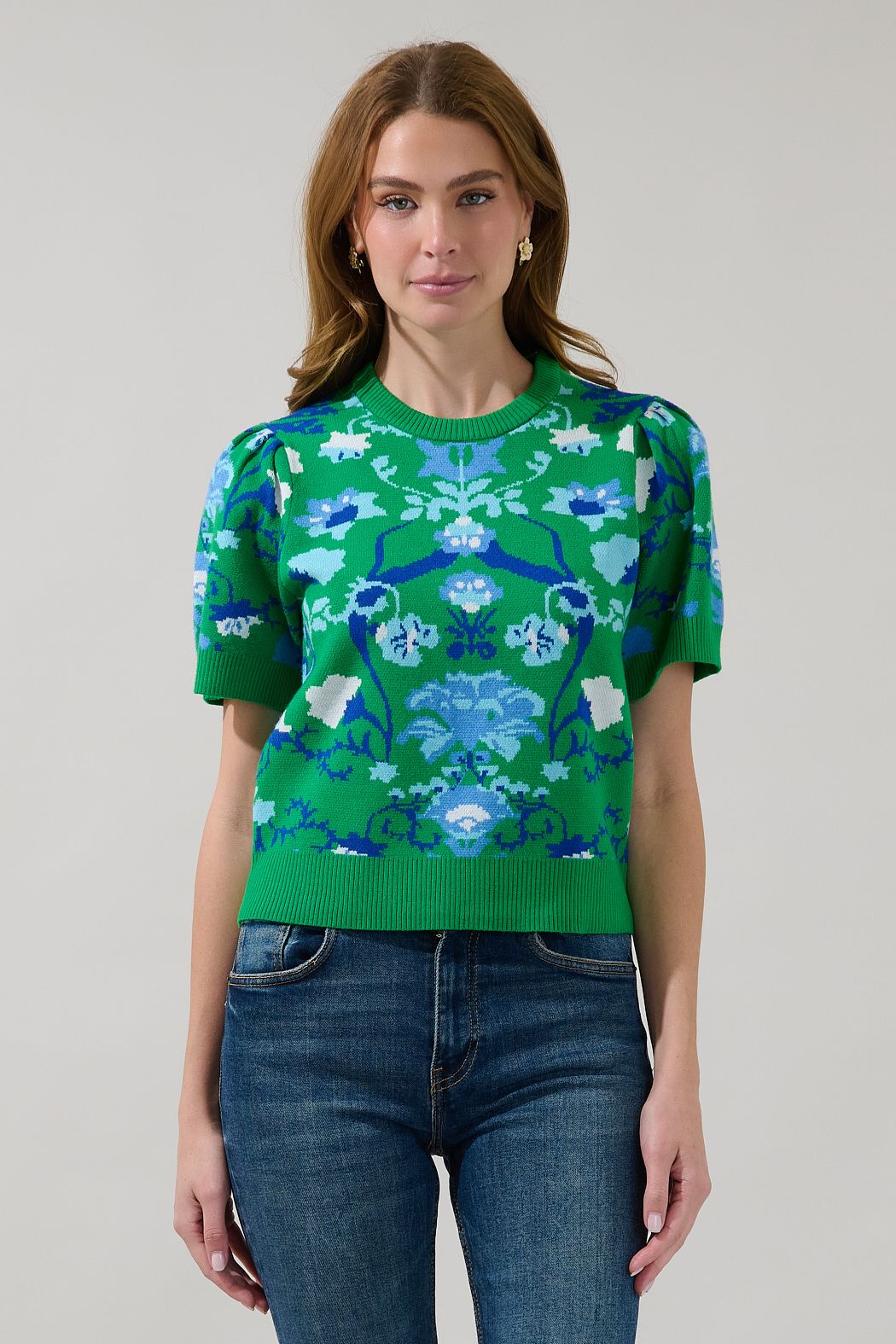 Model wearing a green and blue floral knit sweater with short sleeves, a crew neck, and ribbed trim