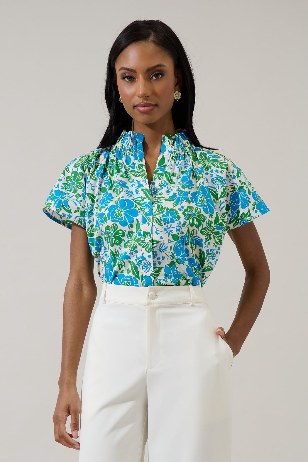 Woman wearing a floral blouse and white pants against a plain background