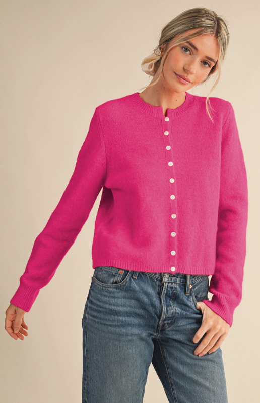 Model wearing a bright pink knit cardigan with white buttons, long sleeves, and ribbed trim, paired with jeans.