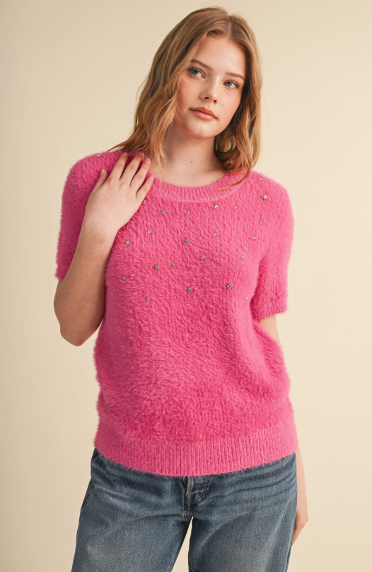 Pink rhinestone-embellished short sleeve sweater with a ribbed crew neckline and relaxed waist-length fit, styled with jeans.