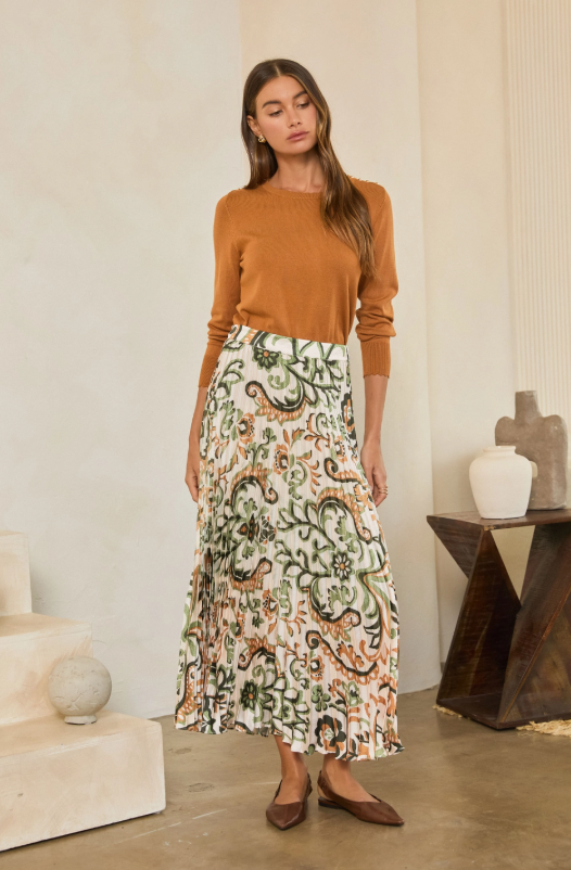 Model wearing a cream pleated maxi skirt with multicolored botanical print, styled with a rust sweater and brown flats.