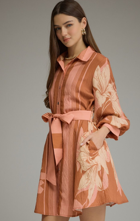 Model wearing a terracotta and blush floral mini shirt dress with long balloon sleeves, a button front, self-tie waist belt, and side pockets.