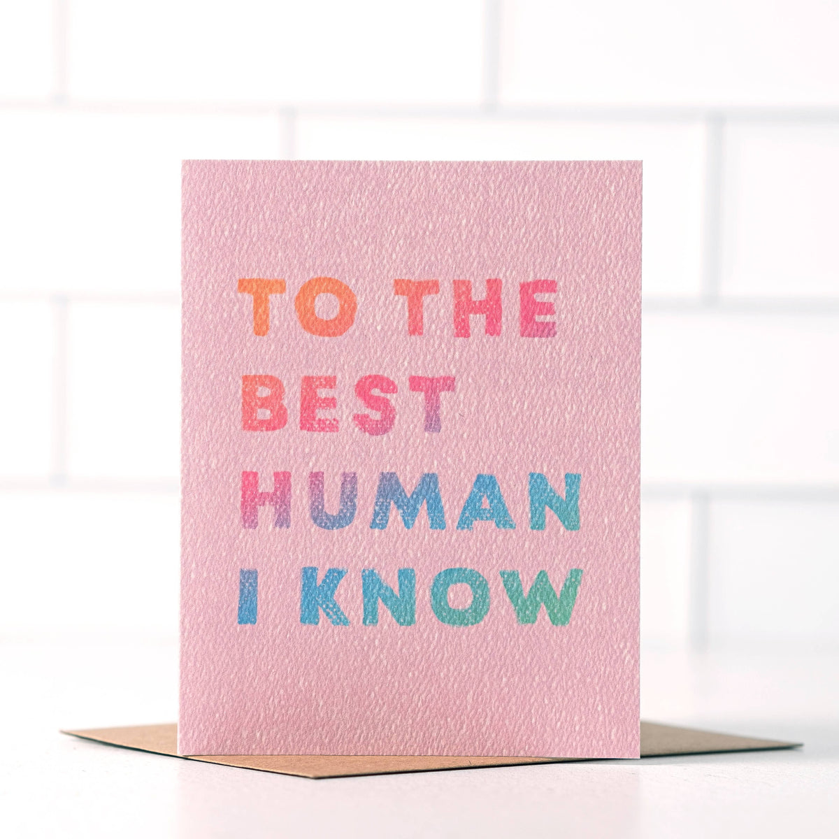 Pink textured greeting card with multicolor “To the Best Human I Know” lettering, displayed with a kraft envelope.
