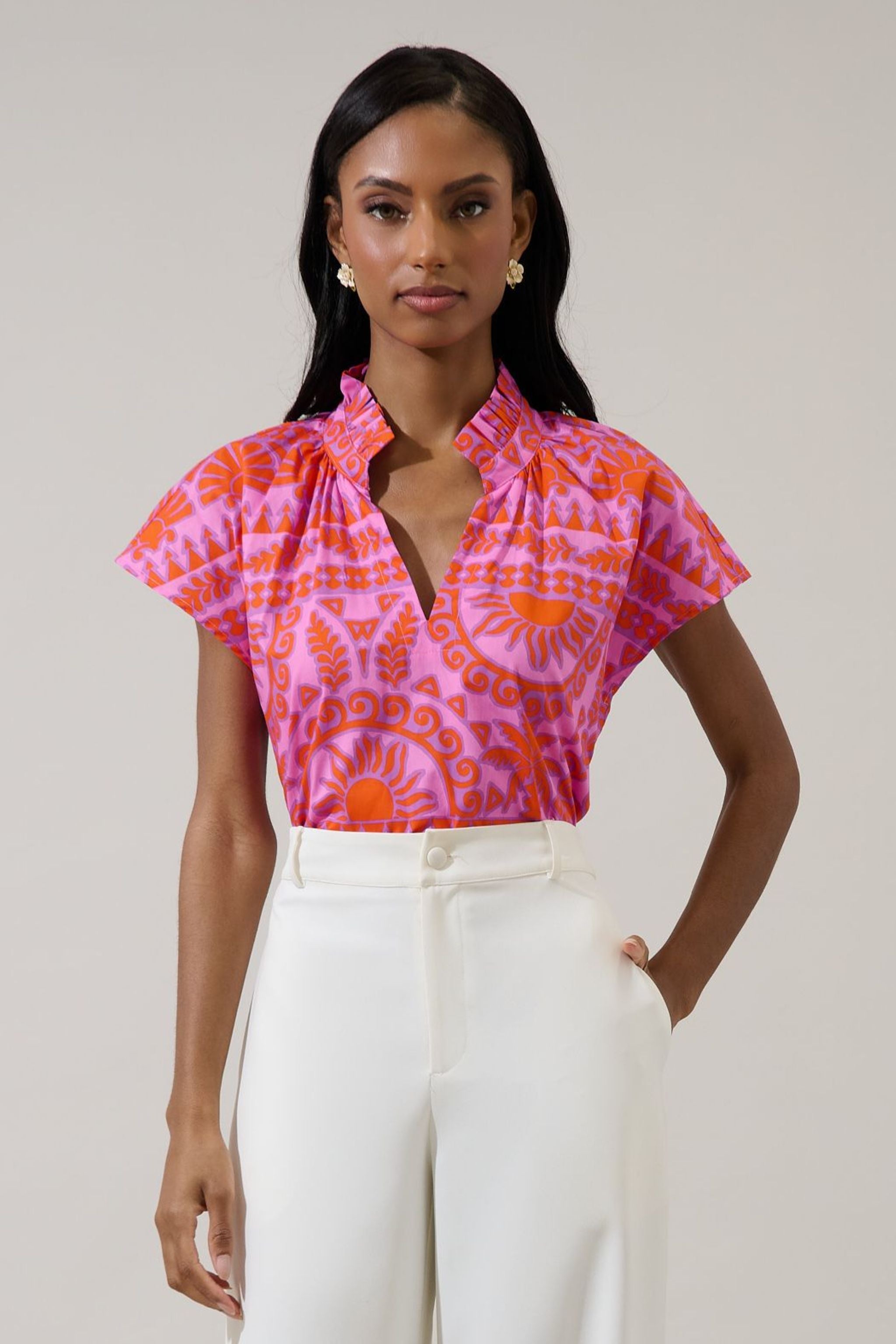 Woman wearing a pink and orange patterned blouse with white pants